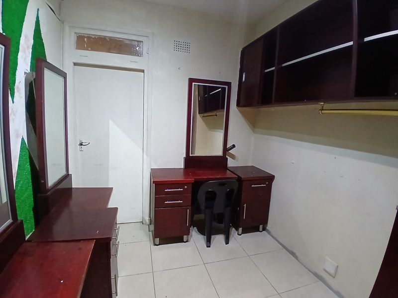 A bedroom featuring built-in dark wood cabinetry and vanity units with tiled flooring, requiring cosmetic updates to improve the overall aesthetic.