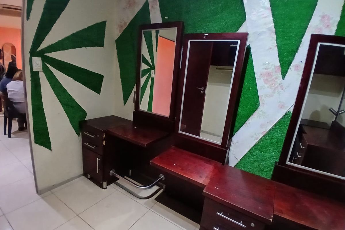 A commercial space featuring built-in vanity stations with integrated mirrors and tiled flooring, currently showing signs of wear on the wall finishes.