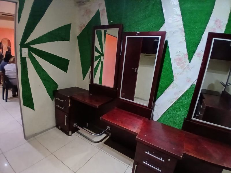 A commercial space featuring built-in vanity stations with integrated mirrors and tiled flooring, currently showing signs of wear on the wall finishes.