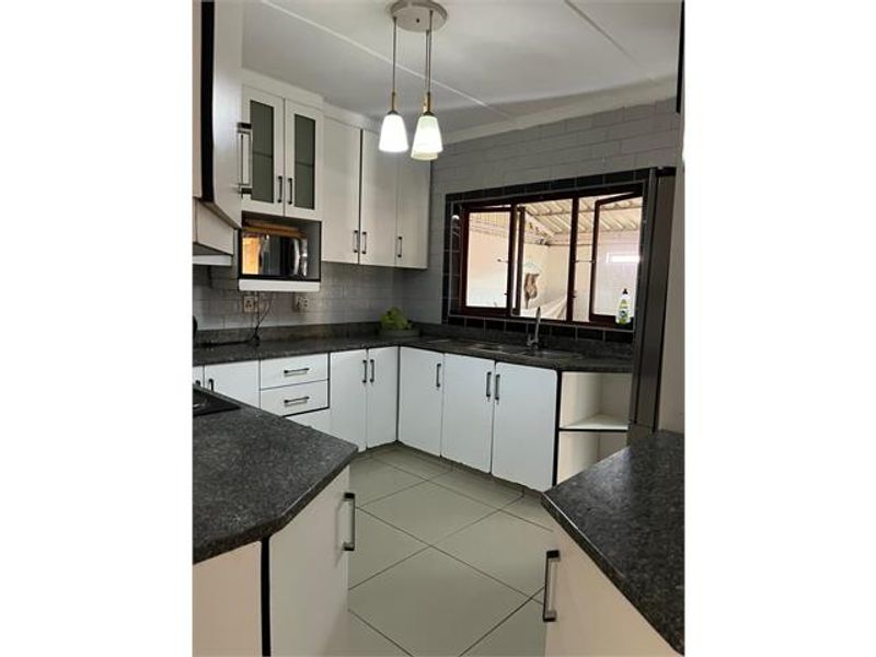 A functional kitchen featuring white cabinetry, dark laminate countertops, tiled backsplash, and a double basin sink with natural light from the window.