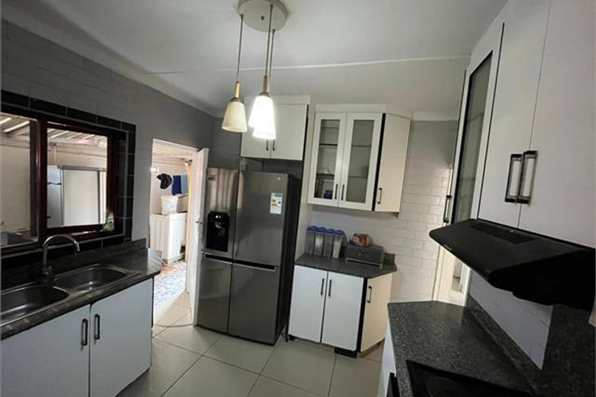 A functional kitchen featuring white cabinetry, dark countertops, a double sink, and an integrated extractor fan with tiled flooring.