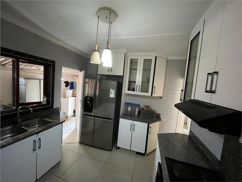 A functional kitchen featuring white cabinetry, dark countertops, a double sink, and an integrated extractor fan with tiled flooring.