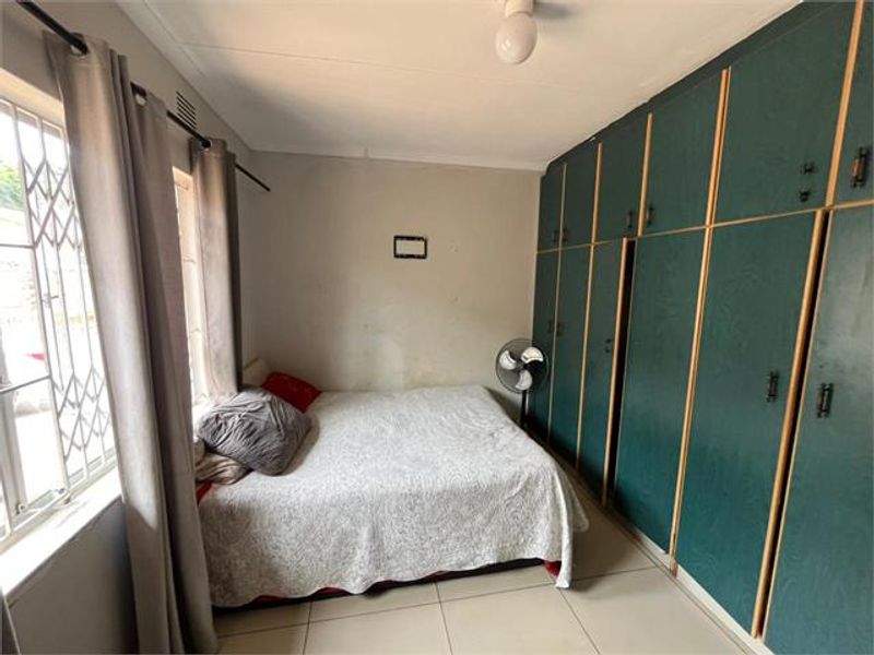 A bedroom featuring tiled flooring, security gates on the windows, and extensive built-in cupboard storage.