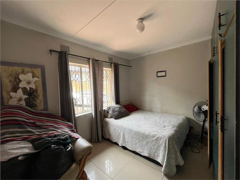 A bedroom featuring tiled flooring, built-in cupboards, and security bars on the window, requiring minor cosmetic updates to the wall finishes.