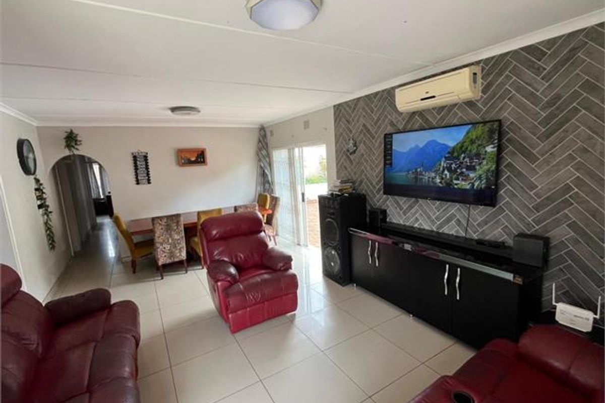 Spacious living area featuring tiled flooring, a decorative herringbone feature wall, and a wall-mounted split-system air conditioner with access to an outdoor area.