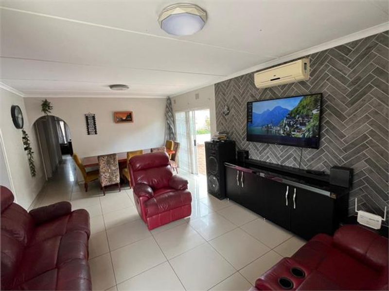 Spacious living area featuring tiled flooring, a decorative herringbone feature wall, and a wall-mounted split-system air conditioner with access to an outdoor area.