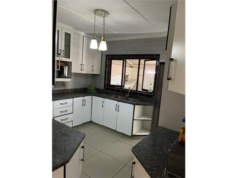 A functional kitchen featuring white cabinetry, dark laminate countertops, tiled backsplash, and tiled flooring, offering a practical layout for daily meal preparation.