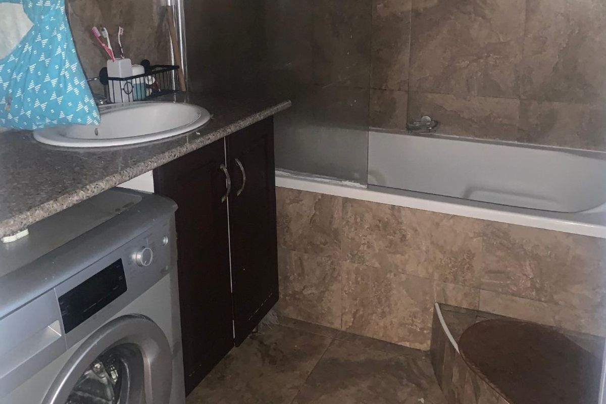 A compact bathroom featuring a vanity with granite countertop, a combined bathtub and shower with glass screen, and full-height wall tiling.