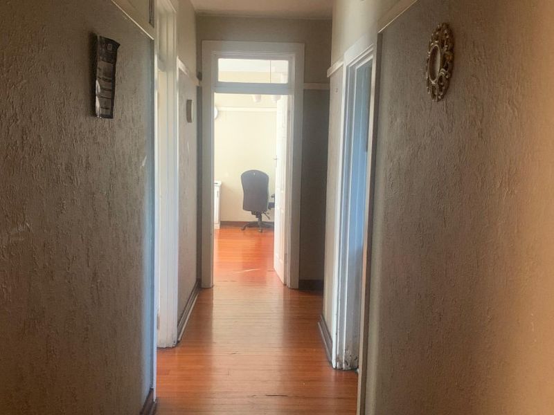 A long interior hallway featuring original hardwood flooring, traditional skirting boards, and multiple doorways leading to adjacent rooms.