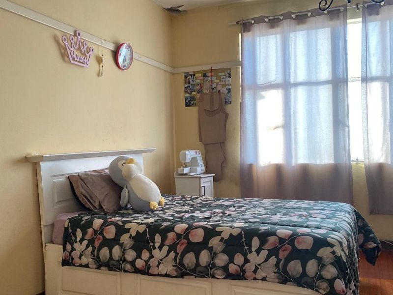 A bedroom featuring original hardwood flooring, a classic picture rail, and a ceiling chandelier, requiring cosmetic updates to the walls and ceiling.