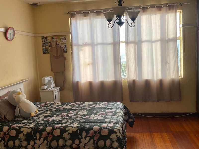 A bedroom featuring original hardwood flooring, a classic ceiling chandelier, and a picture rail, requiring cosmetic updates to the wall finishes.