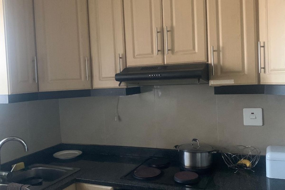 A functional kitchen featuring light-toned cabinetry, dark granite countertops, a built-in oven, electric hob, and an extractor fan.