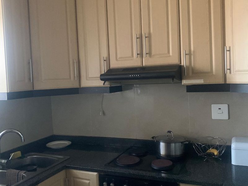 A functional kitchen featuring light-toned cabinetry, dark granite countertops, a built-in oven, electric hob, and an extractor fan.