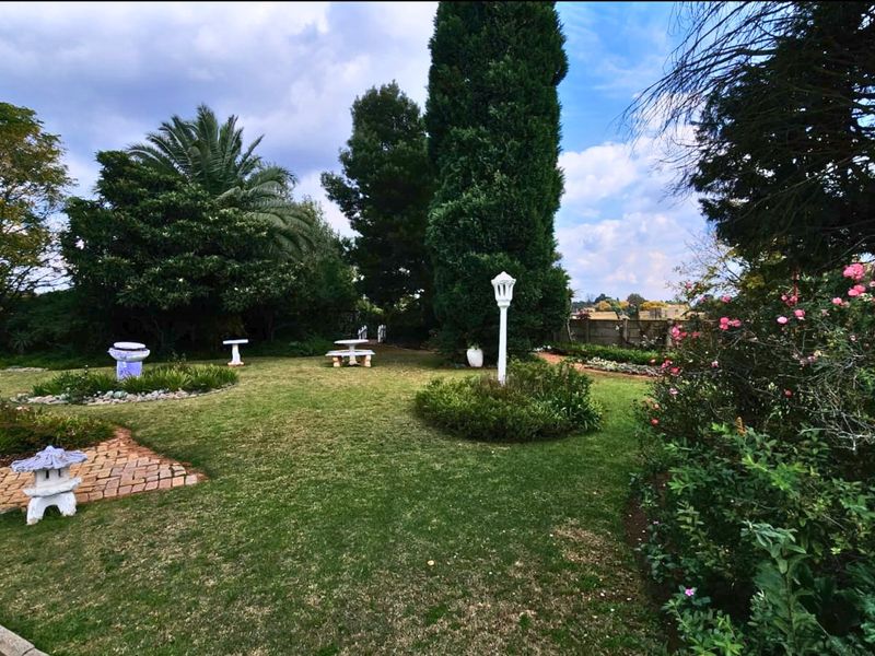 A well-maintained garden featuring mature trees, landscaped lawn areas, brick pathways, and decorative garden lighting.