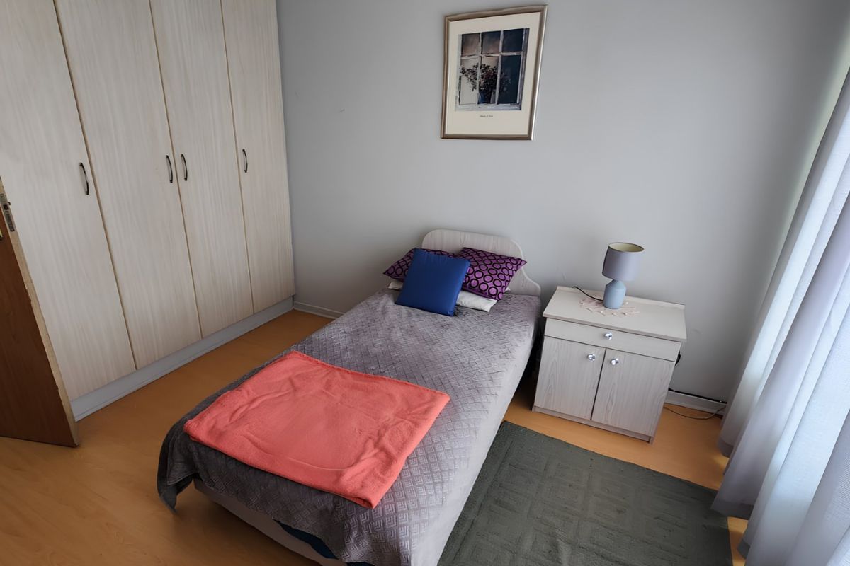 A functional bedroom featuring built-in cupboards and light-toned laminate flooring, providing a clean and practical living space.