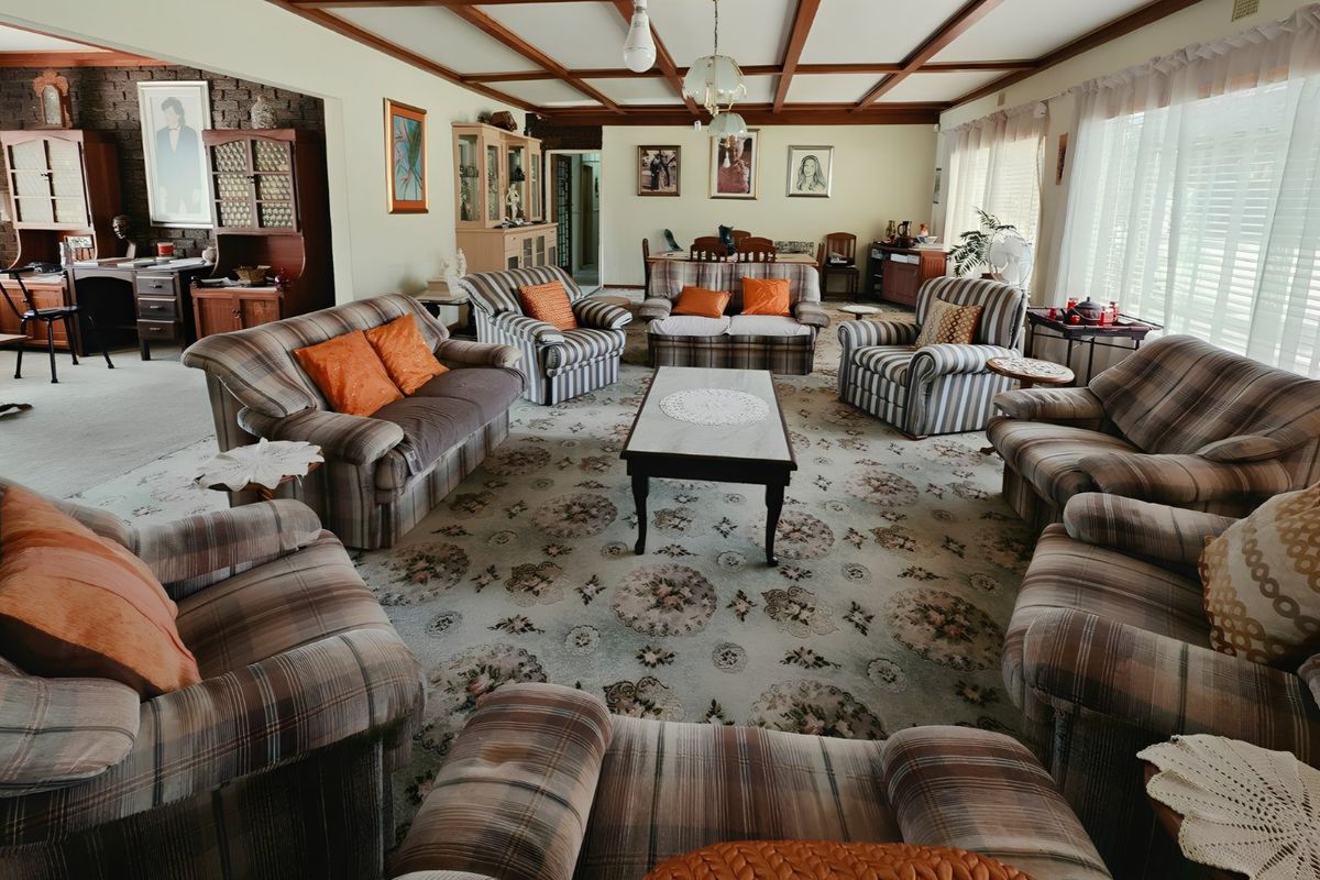 Spacious living room featuring exposed timber ceiling beams, a textured brick feature wall, and wall-to-wall carpeting.