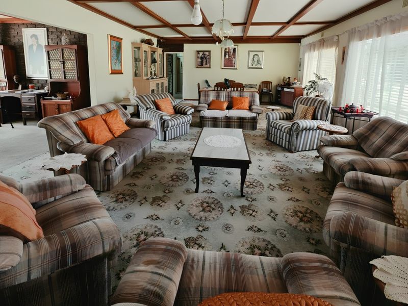 Spacious living room featuring exposed timber ceiling beams, a textured brick feature wall, and wall-to-wall carpeting.