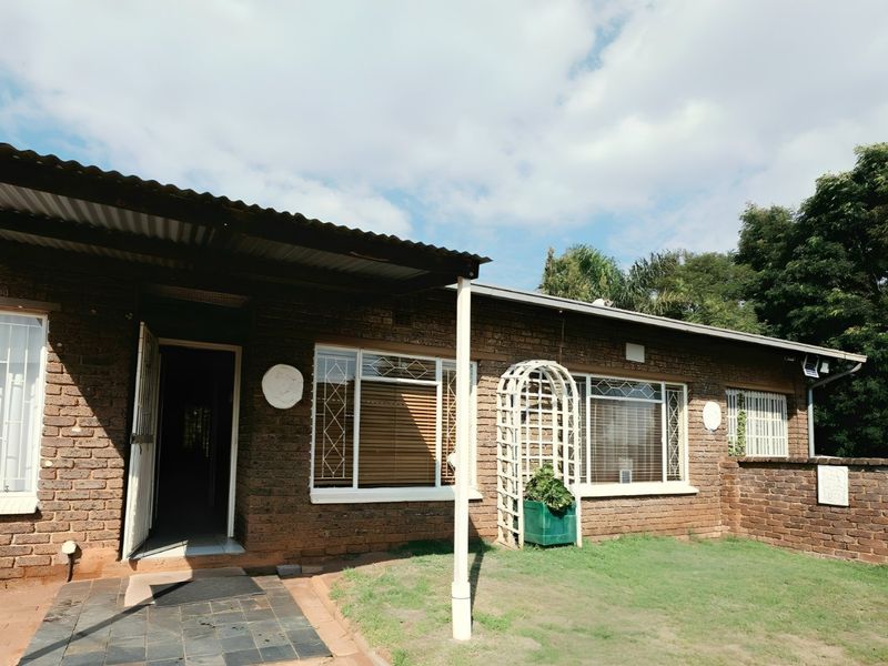 Rear exterior view of a brick house featuring a covered patio area, security bars on windows, and a small garden space.
