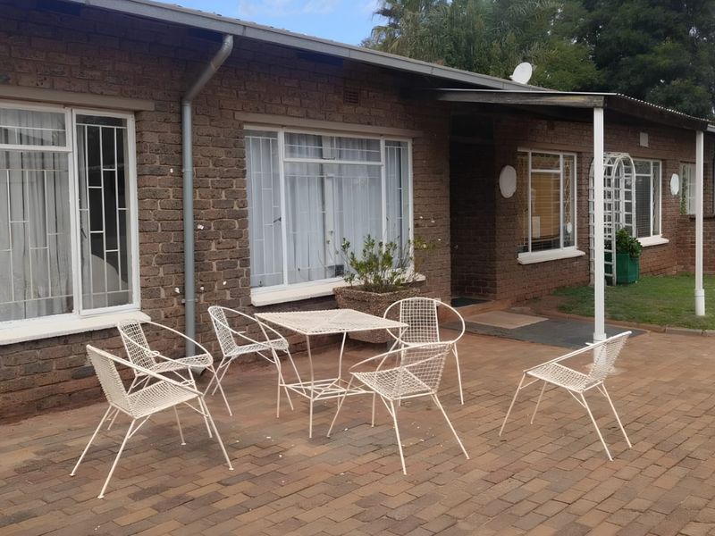A paved outdoor patio area adjacent to a brick-faced house, featuring security bars on windows and functional guttering systems.