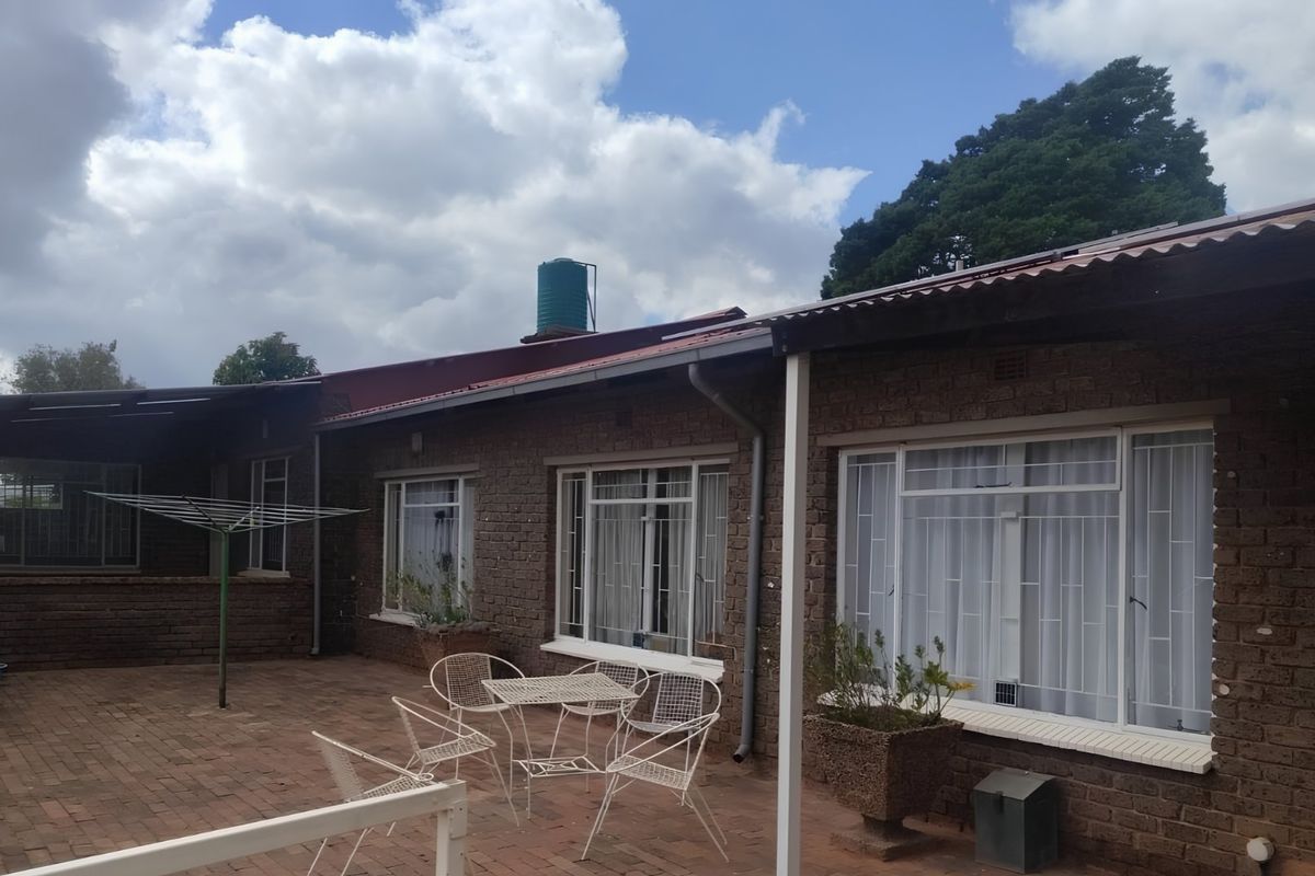 Rear view of the house featuring a brick facade, corrugated metal roof, water tank, and a paved patio area with security bars on windows.