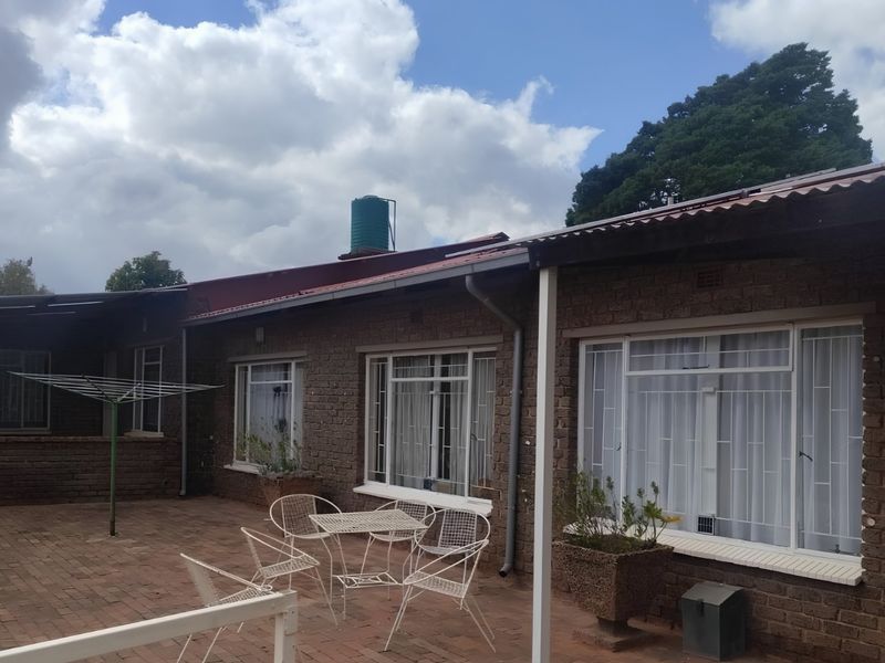Rear view of the house featuring a brick facade, corrugated metal roof, water tank, and a paved patio area with security bars on windows.