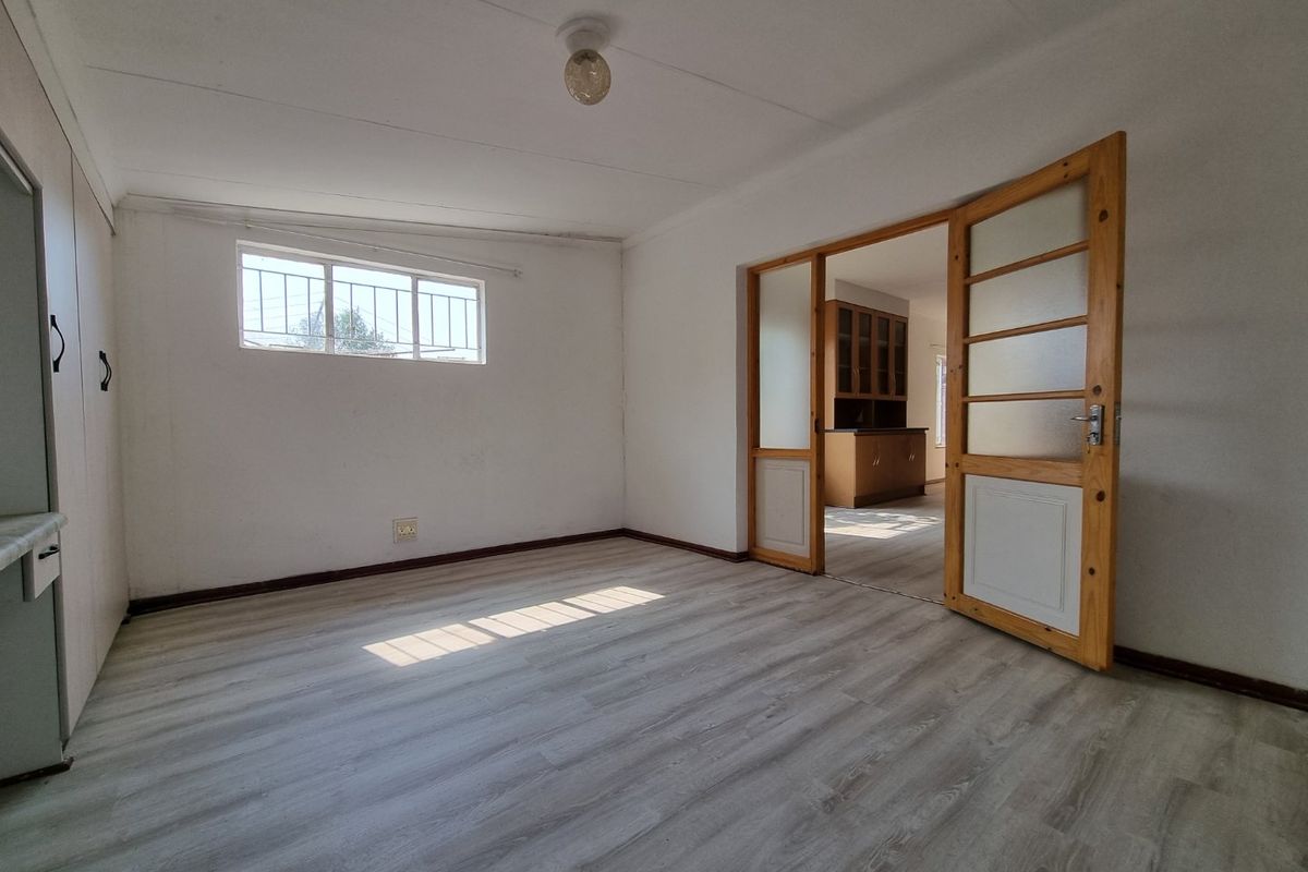 An empty living room featuring light-toned laminate flooring, built-in storage cupboards, and a timber-framed glass door leading to an adjacent room.