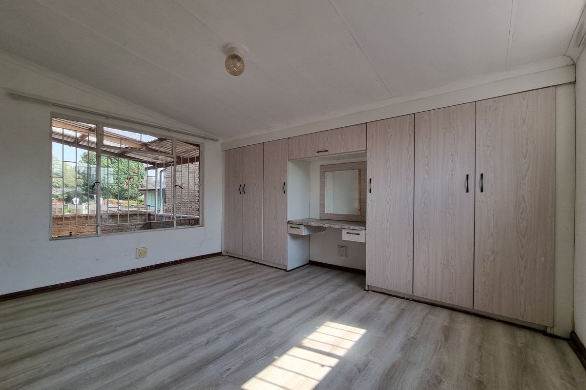 Spacious bedroom featuring light-toned laminate flooring, extensive built-in cabinetry with an integrated vanity, and large windows fitted with security bars.