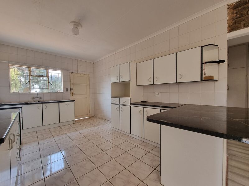 A spacious, empty kitchen featuring white built-in cabinetry, dark laminate countertops, and tiled flooring, offering a blank canvas for modern renovation.