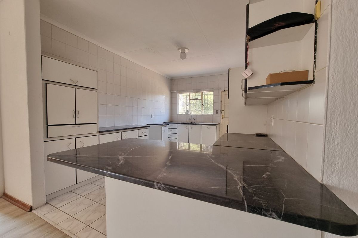 A functional, empty kitchen featuring white built-in cabinetry, dark laminate countertops, tiled backsplash, and tiled flooring, offering a blank canvas for renovation.