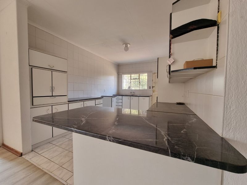 A functional, empty kitchen featuring white built-in cabinetry, dark laminate countertops, tiled backsplash, and tiled flooring, offering a blank canvas for renovation.
