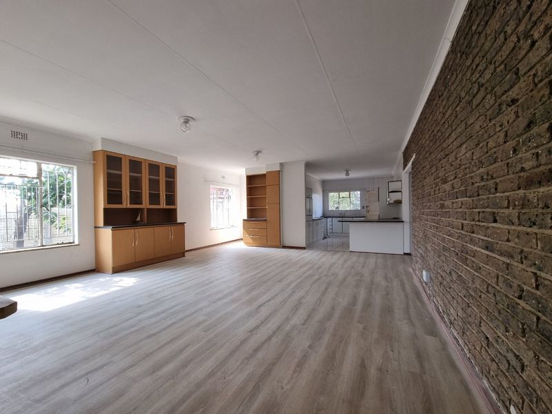 Spacious open-plan living and kitchen area featuring modern laminate flooring, a striking exposed brick feature wall, and ample built-in cabinetry.