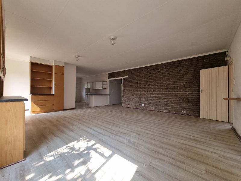 Spacious open-plan living and kitchen area featuring laminate flooring, an exposed brick feature wall, and built-in cabinetry.