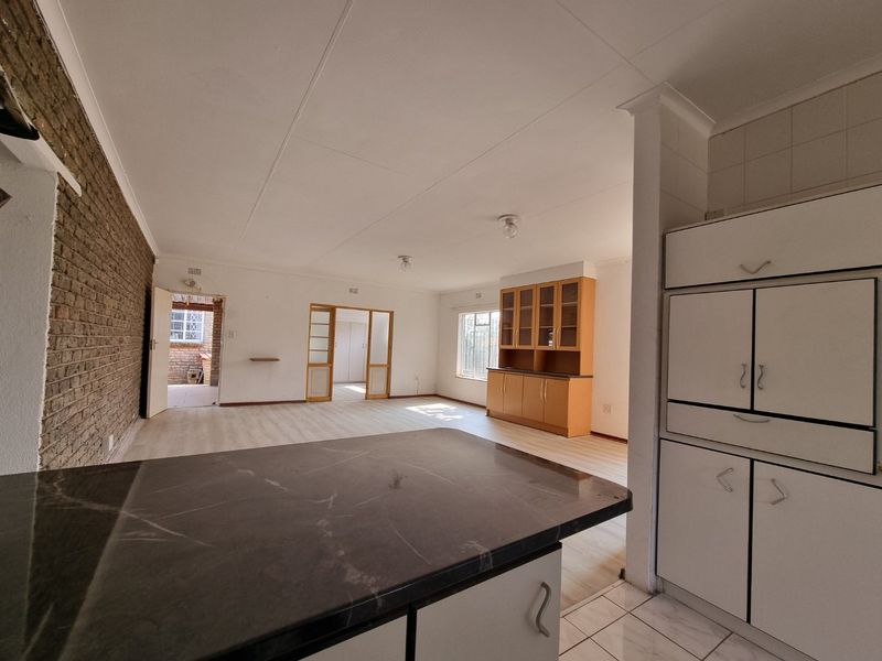 Spacious open-plan living and kitchen area featuring a stone countertop, built-in cabinetry, and an exposed brick feature wall with neutral flooring throughout.