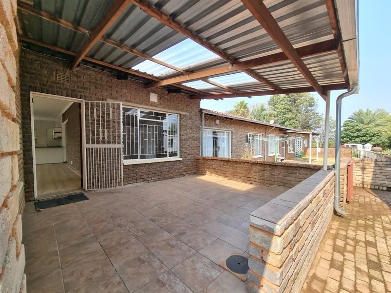 Covered outdoor patio featuring tiled flooring, exposed brick walls, and a corrugated metal roof with translucent panels, providing a functional space for outdoor living.