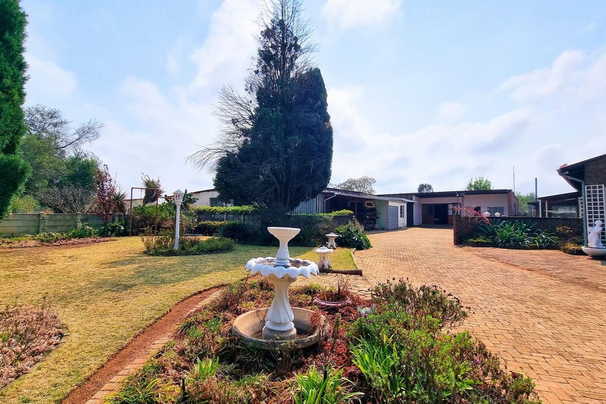 Spacious rear exterior featuring a large brick-paved driveway, established garden with a central fountain, and access to outbuildings.