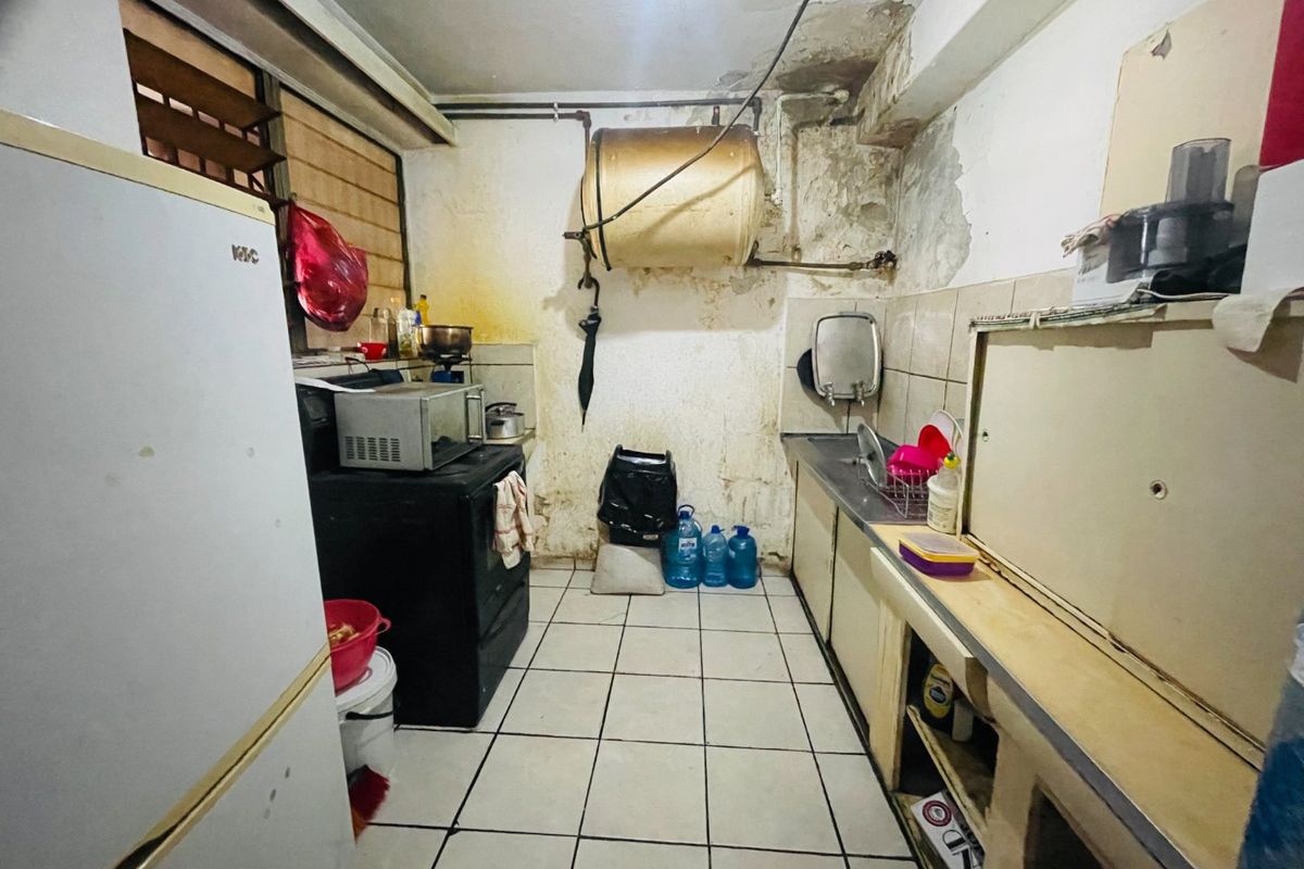 A dated kitchen space requiring significant renovation, featuring tiled flooring, built-in cabinetry, and a wall-mounted water heater with visible wall surface damage.