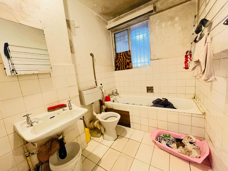 A dated bathroom requiring significant renovation, featuring a bathtub, pedestal basin, and toilet with visible wall and ceiling deterioration.