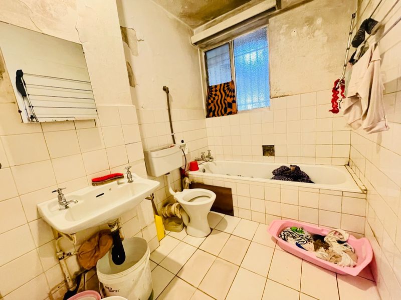 A dated bathroom featuring a bathtub, pedestal basin, and toilet, requiring significant renovation and repair to the wall finishes and overall infrastructure.