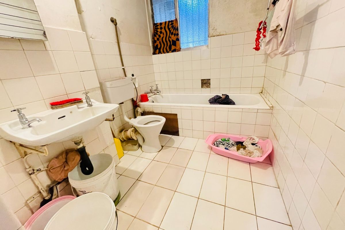 A dated bathroom featuring a pedestal basin, toilet, and bathtub with full-height wall tiling, requiring significant renovation and modernization of fixtures and finishes.