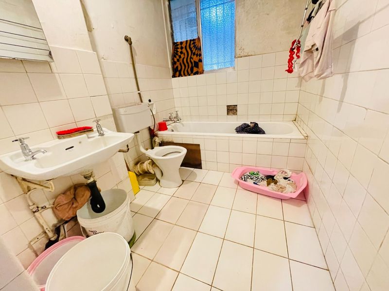 A dated bathroom featuring a pedestal basin, toilet, and bathtub with full-height wall tiling, requiring significant renovation and modernization of fixtures and finishes.