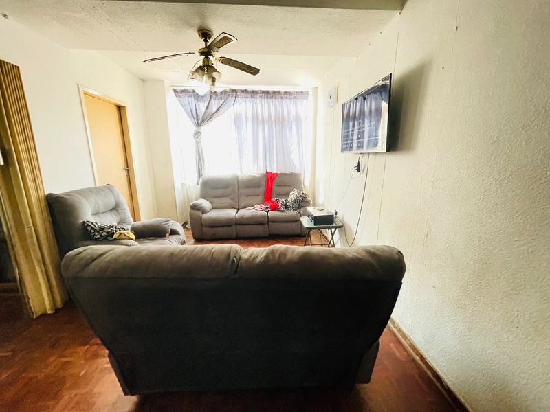 A living room featuring parquet flooring and a ceiling fan, with visible wear on the wall surfaces.