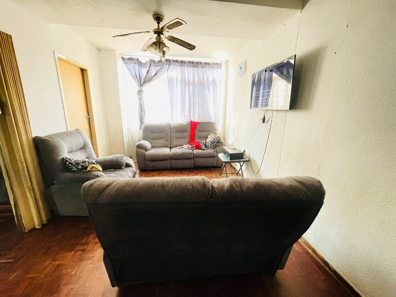 A living room featuring parquet flooring and a ceiling fan, with visible wall imperfections requiring cosmetic attention.