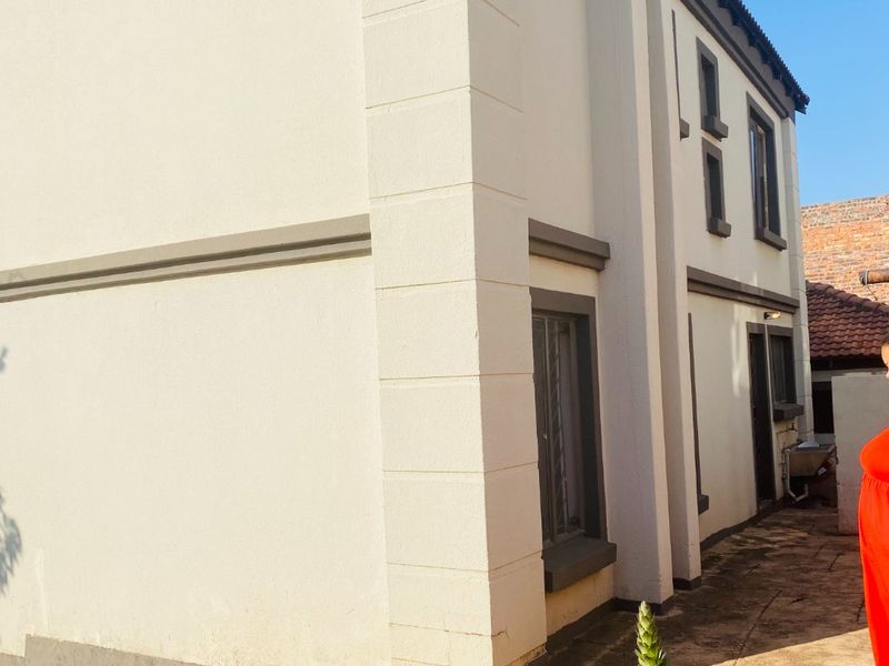 A side view of the property showing the plastered exterior facade, tiled roof, and paved walkway area.