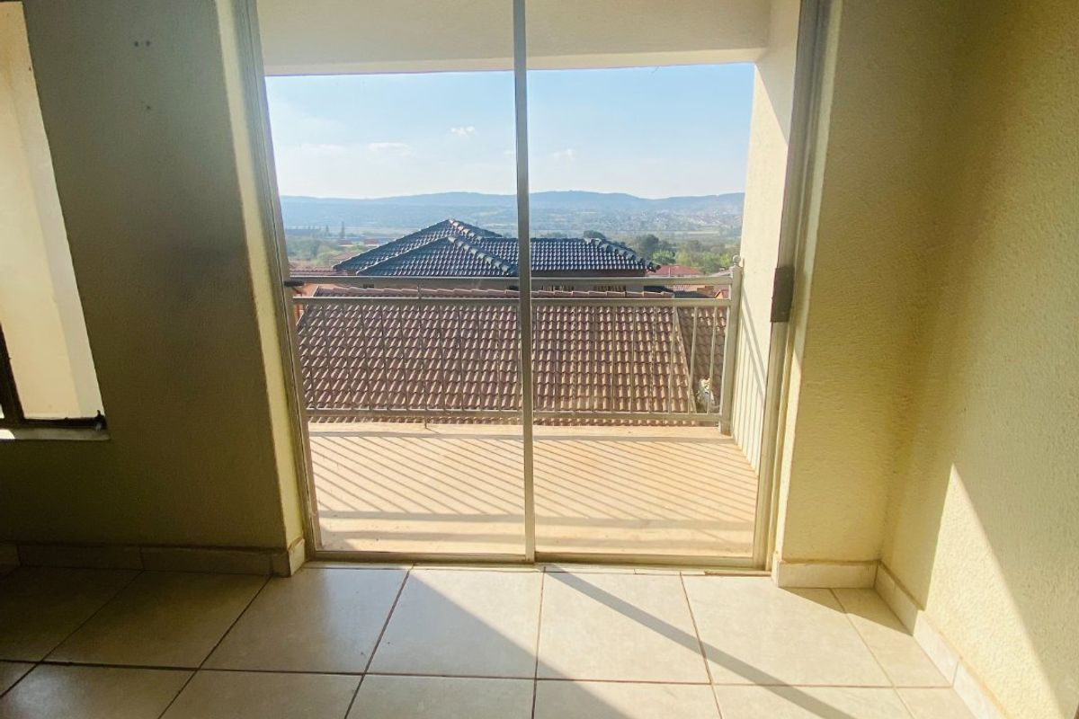 An empty living area featuring tiled flooring and a sliding glass door that opens onto a balcony with scenic views.