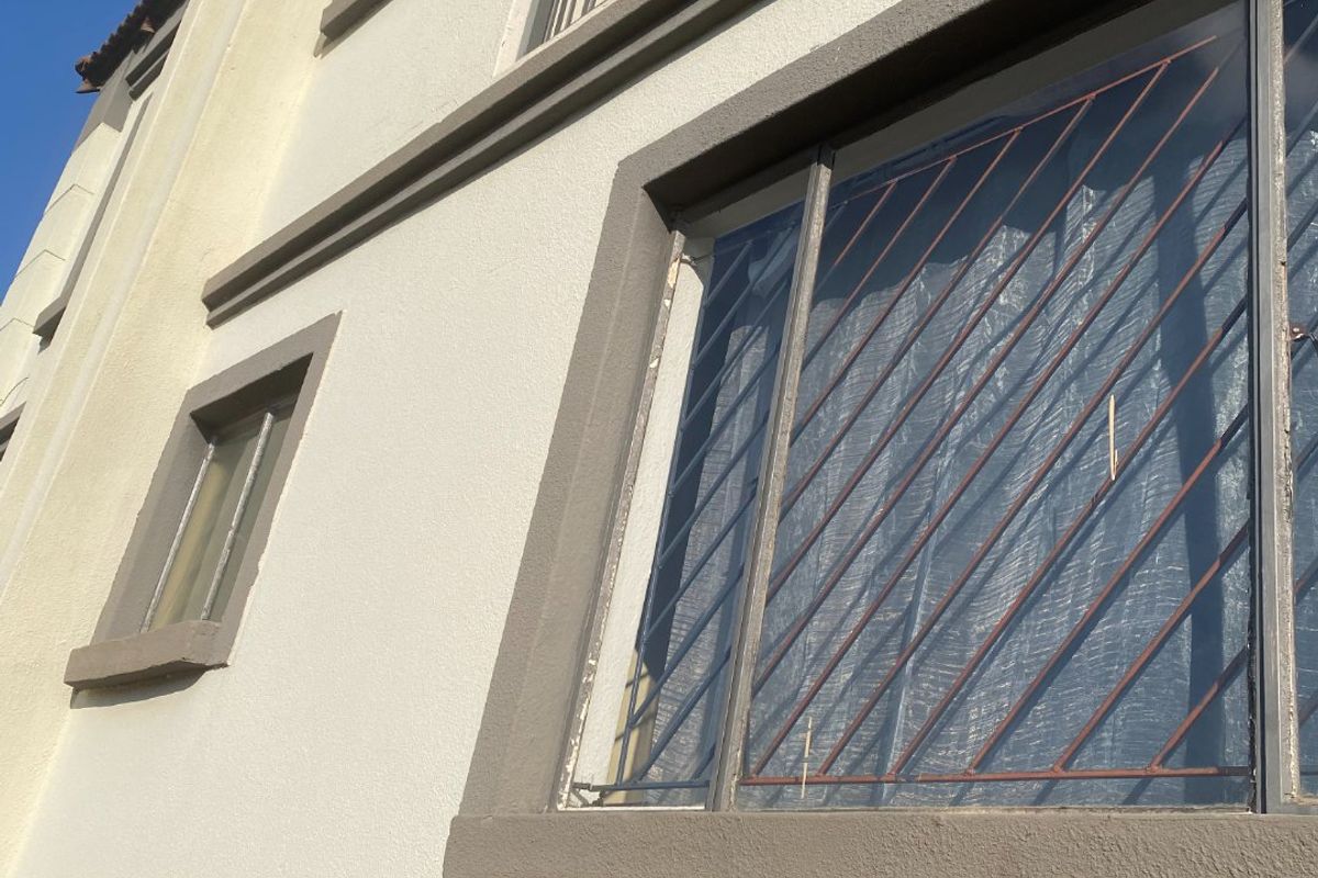 Exterior view of the building facade featuring a balcony with metal railings and windows fitted with security bars.