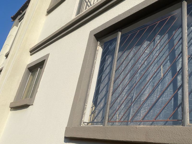 Exterior view of the building facade featuring a balcony with metal railings and windows fitted with security bars.