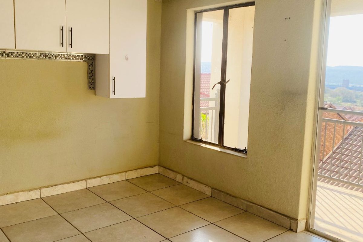 An empty kitchen area featuring tiled flooring, wall-mounted cabinetry, and a sliding glass door leading to an outdoor balcony.