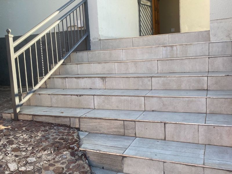 Exterior entrance featuring a tiled staircase with a metal handrail and a security gate leading to the main timber front door.