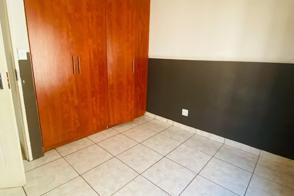 A vacant bedroom featuring tiled flooring, a built-in wooden wardrobe, and two-tone wall paint with decorative chair rail molding.
