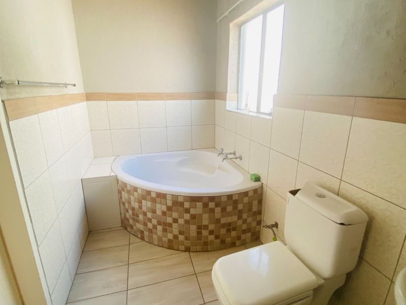 A bathroom featuring a corner bathtub and toilet, with tiled finishes. The room requires completion of wall plastering and ceiling installation.